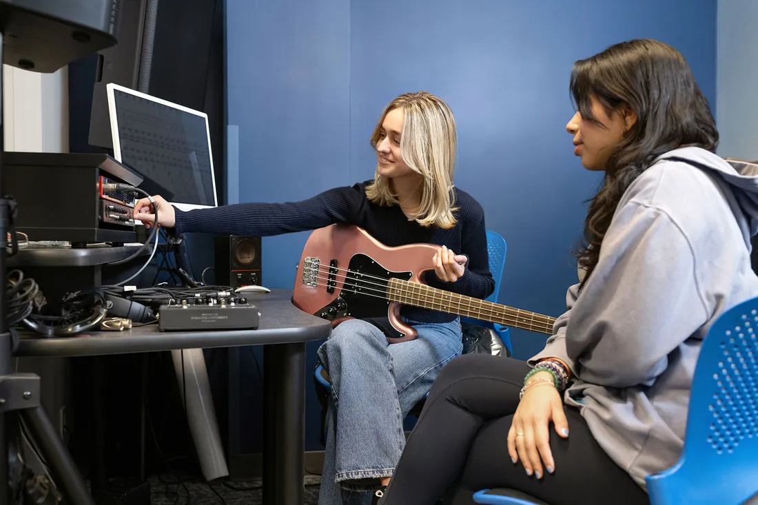 Students sitting at computer making music with guitar.