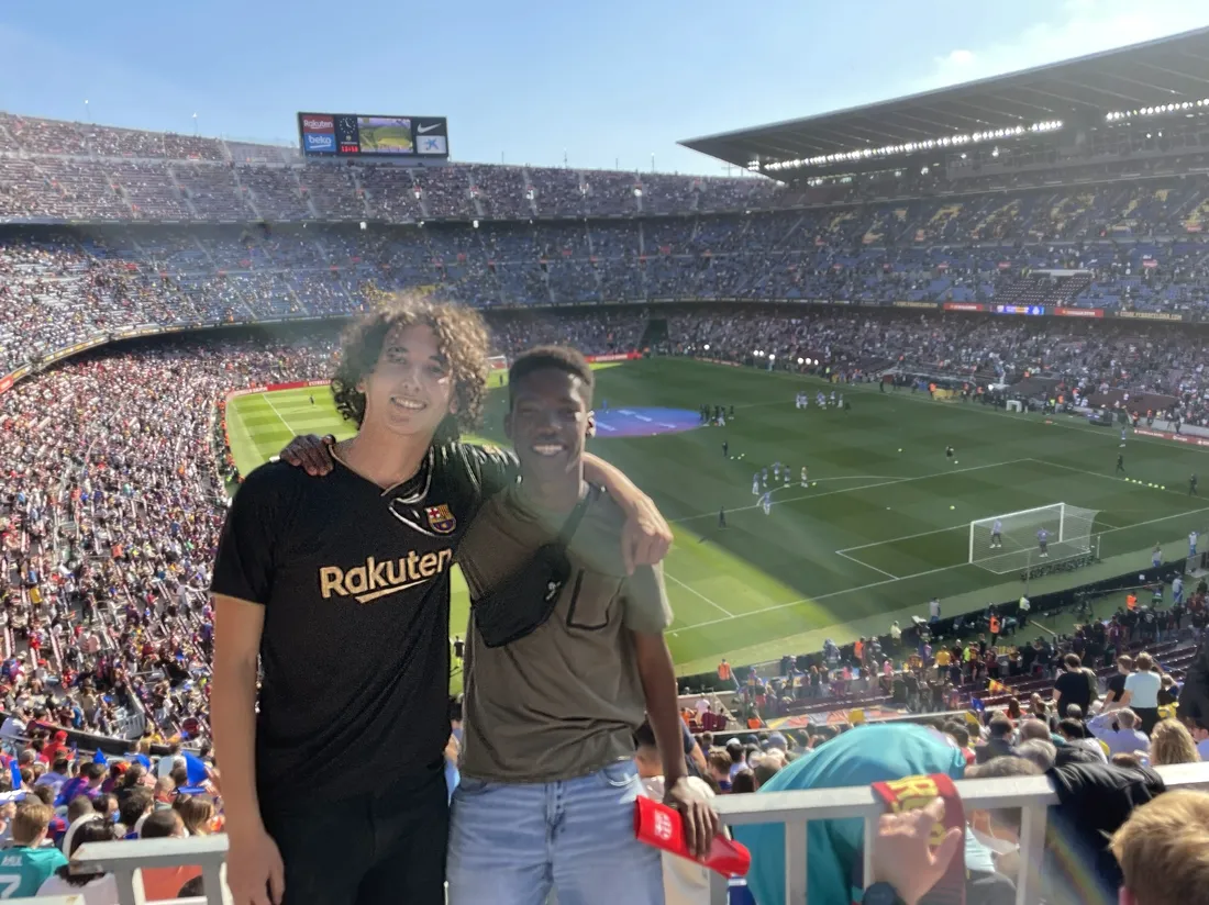 Adam Baltaxe standing and smiling with a friend at a football game in Barcelona, Spain.